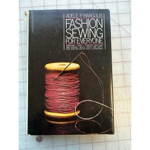 May include: A vintage book cover for "Fashion Sewing for Everyone" by Adele P. Margolis. The cover features a spool of red thread with a needle, set against a black background. The book promises simplified sewing instructions.