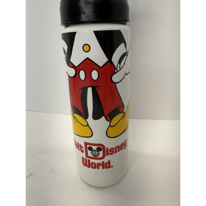 May include: White water bottle featuring a graphic of Mickey Mouse's torso, with black arms, red shorts, and yellow shoes. The bottle has a black lid and the words "Walt Disney World" are printed on the bottom.