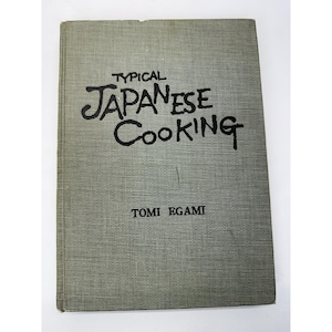 May include: A vintage cookbook titled "Typical Japanese Cooking" by Tomi Egami. The book has a textured, gray cover with the title and author's name in black lettering. The cover is slightly worn, suggesting its age.