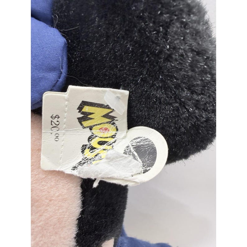 May include: A black plush toy with a blue outfit and a tag that says "Mouse". The tag has a price of $20.00. The toy has a fluffy texture.