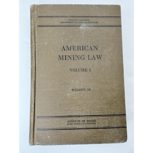 May include: A vintage book titled "American Mining Law, Volume 1" with the text "Bulletin 123." The cover is a faded tan color with black text. The book is from the State of California, Department of Natural Resources, Division of Mines.