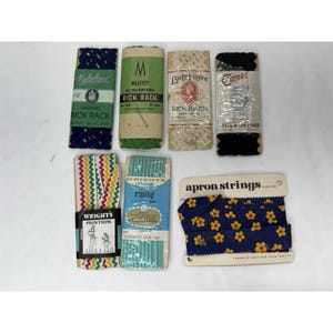 May include: A collection of vintage sewing notions, including various rolls of rick rack, piping, and apron strings. The rick rack comes in navy, green, and cream colors. The apron strings are navy blue with yellow floral patterns.