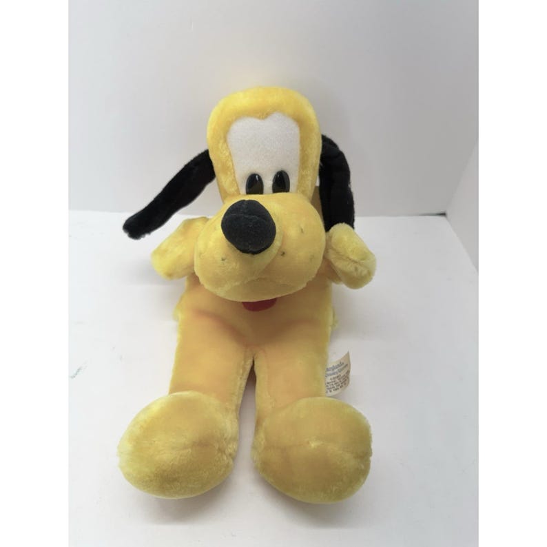 Puede incluir: Un juguete de peluche con forma de perro amarillo con orejas y nariz negras. El perro tiene una cara blanca y un collar rojo. El juguete es suave y tierno, para ni&ntilde;os.