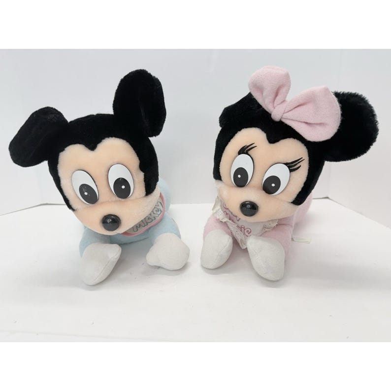 Puede incluir: Se muestran dos personajes de peluche de Disney, Mickey Mouse y Minnie Mouse. Mickey lleva un atuendo azul y Minnie un atuendo rosa con un lazo. Ambos tienen orejas negras y ojos grandes. Los juguetes est&aacute;n sobre una superficie blanca.