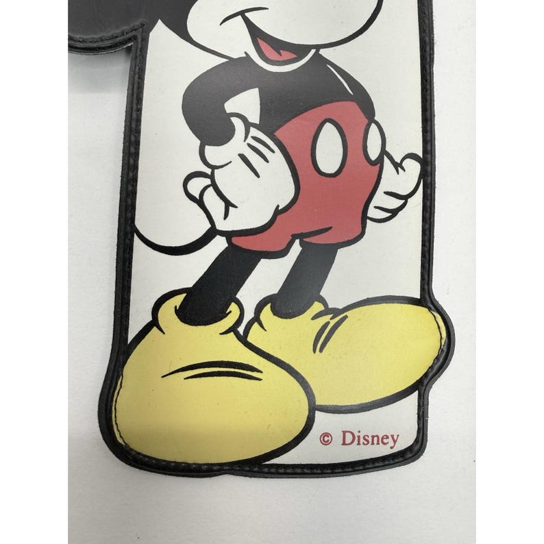 May include: A rectangular, white and black accessory featuring a smiling Mickey Mouse illustration. Mickey is wearing red shorts, yellow shoes, and white gloves. The Disney logo is printed at the bottom.