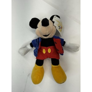 Peut inclure: Peluche de Mickey Mouse avec une veste bleue, un short rouge et des chaussures jaunes. La peluche a des oreilles noires, un nez noir et des gants blancs. Une &eacute;tiquette est attach&eacute;e.