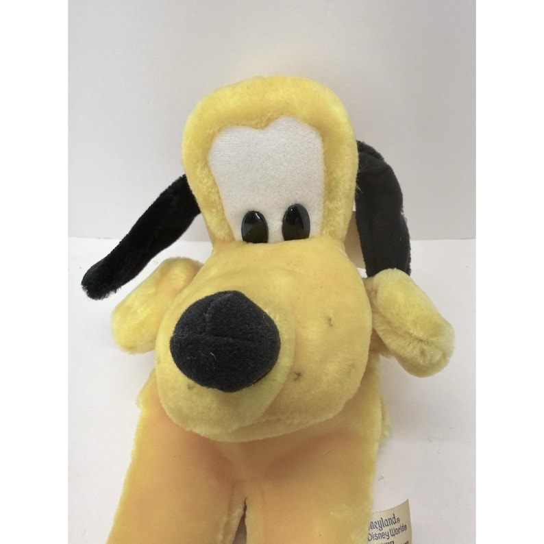 Puede incluir: Un peluche de Pluto, un perro amarillo con orejas negras y una nariz negra. El juguete tiene una cara blanca y ojos negros. El juguete est&aacute; hecho de material suave y afelpado.