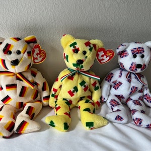 May include: Three plush beanie baby bears with different country flags printed on them. The bear on the left is wearing a German flag pattern, the middle bear is wearing a Mexican flag pattern, and the bear on the right is wearing a British flag pattern.
