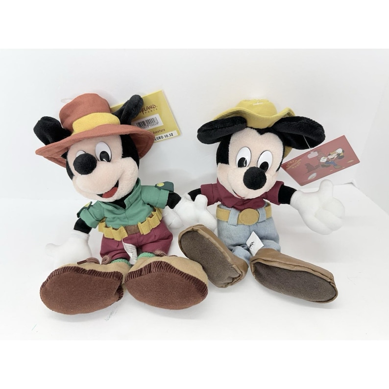 K&ouml;nnte beinhalten: Zwei Mickey Mouse-Pl&uuml;schtiere in Cowboy-Outfits. Einer tr&auml;gt ein gr&uuml;nes Hemd und eine weinrote Hose, der andere ein rotes Hemd und blaue Jeans. Beide haben braune Schuhe und wei&szlig;e Handschuhe.