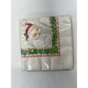 May include: A package of white paper napkins with a red and green border. The napkins feature a printed image of Santa Claus's face.