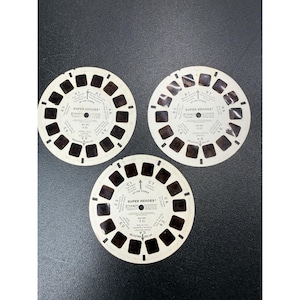 May include: Three circular white View-Master reels labeled Super Heroes, each featuring seven pairs of small rectangular film frames arranged around the perimeter with printed text identifying scenes A1 through A7, B1 through B7, and C1 through C7.