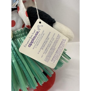 Puede incluir: Un peluche de vaca con un dise&ntilde;o de lunares rojos y blancos, una falda verde y una etiqueta que dice "Everyone loves to get applause". El juguete tiene pelaje blanco y negro y est&aacute; fabricado por Applause Inc.