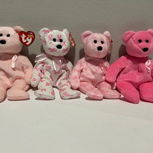May include: Four pink and white beanie baby bears with pink ribbons. The bears are all wearing the Ty Beanie Babies tag.