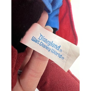 May include: A red, blue, and black plush toy with a white tag that reads "Disneyland&reg; Walt Disney World&reg;".
