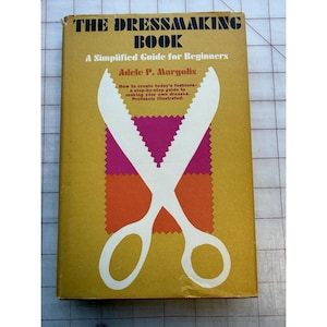 May include: A vintage book titled "THE DRESSMAKING BOOK" with a yellow cover. The cover features white scissors over a pink and orange fabric design. The book is a guide for beginners by Adele P. Margolis, with instructions on creating fashions.