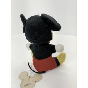 Puede incluir: Un peluche vintage de Mickey Mouse, con cabeza y orejas negras, torso negro, pantalones cortos rojos, pies amarillos y guantes blancos. El juguete tiene una etiqueta que dice "Goldblatt's". El peluche est&aacute; sentado.
