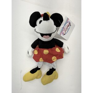 Puede incluir: Un peluche de Minnie Mouse. El peluche tiene una cara blanca, orejas negras y una falda roja con lunares amarillos. Tiene zapatos amarillos y guantes blancos. Una etiqueta de Disney Store est&aacute; adjunta.