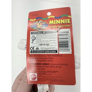 Puede incluir: Una etiqueta roja de juguete Minnie Mouse "Cuddly Collectible" con guantes blancos. La etiqueta incluye el texto "Minnie" y "Mickey's Stuff". La etiqueta tambi&eacute;n incluye informaci&oacute;n para el consumidor y requisitos de seguridad.