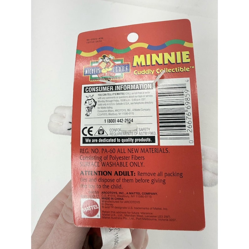 Puede incluir: Una etiqueta roja de juguete Minnie Mouse "Cuddly Collectible" con guantes blancos. La etiqueta incluye el texto "Minnie" y "Mickey's Stuff". La etiqueta tambi&eacute;n incluye informaci&oacute;n para el consumidor y requisitos de seguridad.