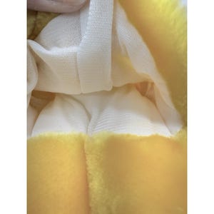 Puede incluir: Primer plano de un juguete de peluche amarillo con un forro de malla blanca. El exterior amarillo tiene una textura suave y difusa. El forro blanco es visible dentro del juguete.
