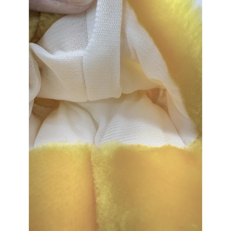 Puede incluir: Primer plano de un juguete de peluche amarillo con un forro de malla blanca. El exterior amarillo tiene una textura suave y difusa. El forro blanco es visible dentro del juguete.