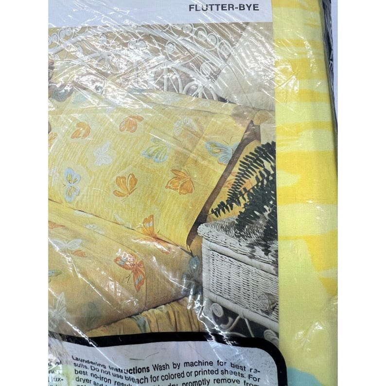 May include: Yellow and white striped packaging with the text "FLUTTER-BYE" at the top. The packaging shows a yellow bedspread with a butterfly pattern and a white wicker bedside table.