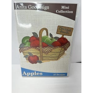 May include: A clear plastic case featuring an embroidered design of a basket filled with red and green apples. The text "Anita Goodesign Mini Collection" is at the top, with "Apples" and "27 Designs" at the bottom. A small sign reads "Orchard Fresh."