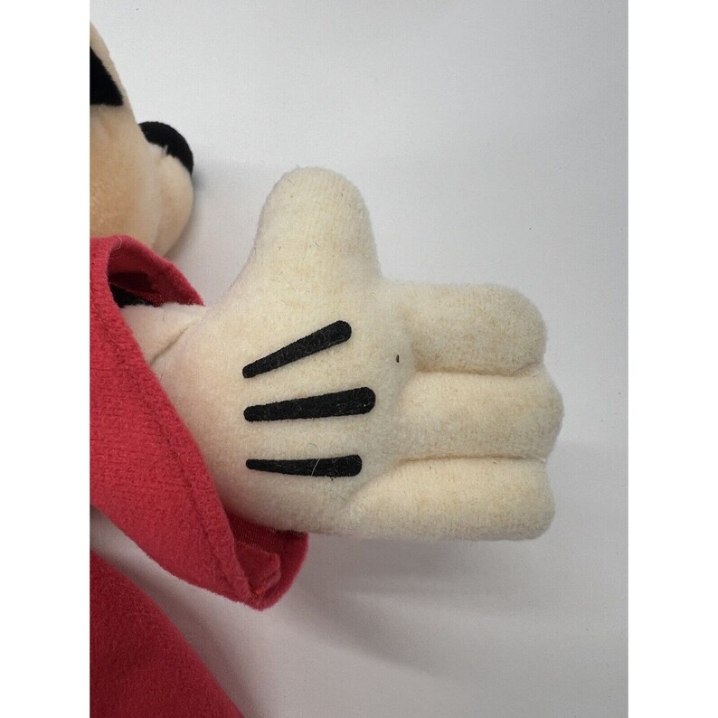 May include: A plush toy with a red jacket and white gloves. The toy has black eyes and a black nose. The toy is in a sitting position with its right hand raised.