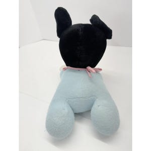 Puede incluir: Un perro de peluche con cabeza y orejas negras y cuerpo azul claro. El perro tiene una cinta rosa atada al cuello. Un juguete suave para ni&ntilde;os.