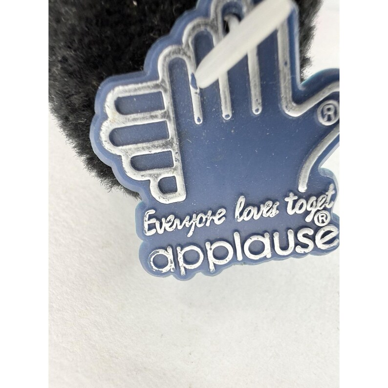 May include: A blue foam hand-shaped tag with the text "Everyone loves toget applause" in white lettering. The tag has a white string attached and is partially obscured by a black, fuzzy material.