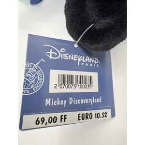 May include: A black plush toy with a blue and white accent. A blue tag is attached, featuring the Disneyland Paris logo and the text "Mickey Discoveryland". The tag also includes a barcode.