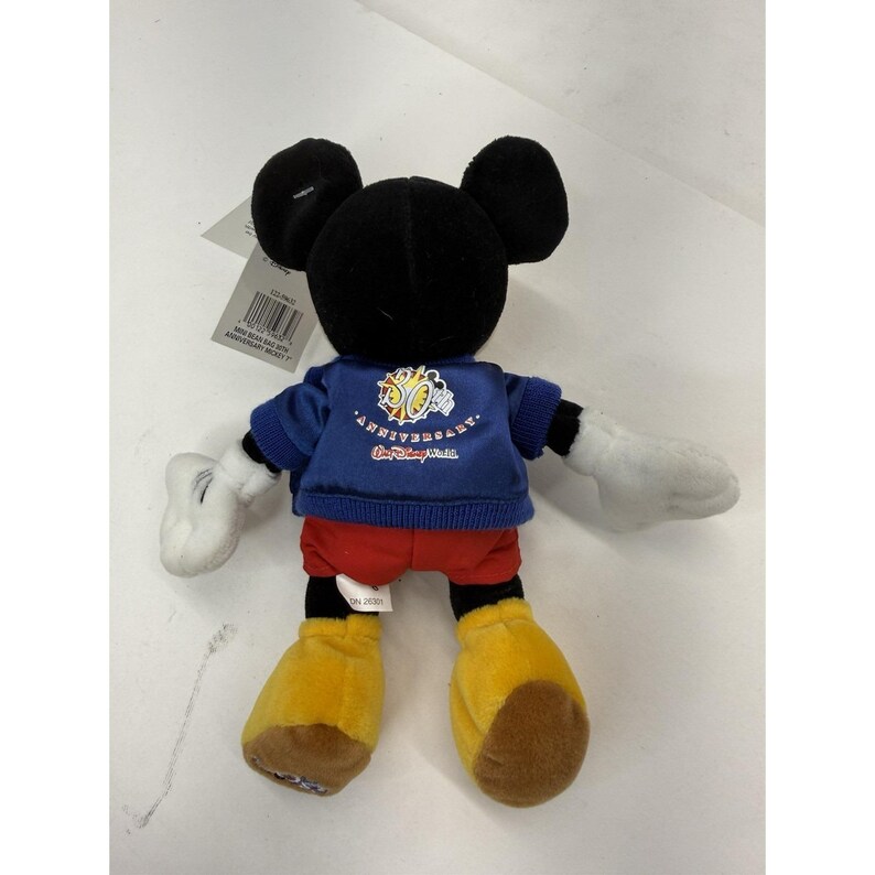 Peut inclure: Poup&eacute;e en peluche Mickey Mouse avec oreilles et t&ecirc;te noires, gants blancs et chaussures jaunes. La poup&eacute;e porte une veste bleue avec un logo du 50e anniversaire et un short rouge. Une &eacute;tiquette est attach&eacute;e.