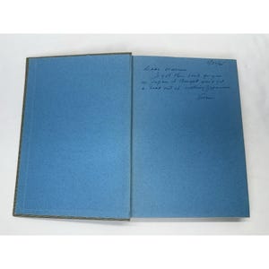 May include: An open book with blue pages and a dark spine. Handwritten text in blue ink on the right page reads "Dear Warren, I got the book for you in Japan I thought you'd get a kick out of cooking Japanese, from..."