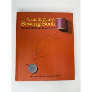 May include: An orange-colored book titled "Coats & Clark's Sewing Book" with the subtitle "Newest Methods from A to Z." The cover features a spool of purple thread and a gray button with thread. The book is a revised and expanded edition.