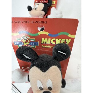 Puede incluir: Primer plano de dos peluches de Mickey Mouse. Los juguetes tienen orejas negras, cara beige y manos blancas. Un juguete est&aacute; en primer plano y el otro en segundo plano. Est&aacute;n unidos a un respaldo de cart&oacute;n rojo con las palabras "Mickey's Stuff" y "Mickey Cuddly C" impresas.