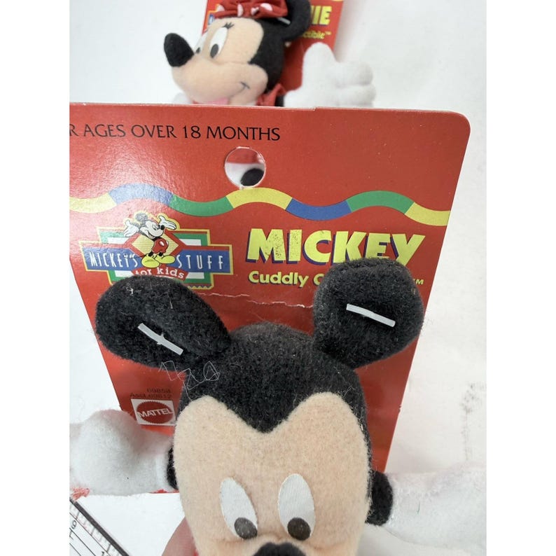 Puede incluir: Primer plano de dos peluches de Mickey Mouse. Los juguetes tienen orejas negras, cara beige y manos blancas. Un juguete est&aacute; en primer plano y el otro en segundo plano. Est&aacute;n unidos a un respaldo de cart&oacute;n rojo con las palabras "Mickey's Stuff" y "Mickey Cuddly C" impresas.