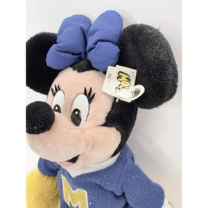 May include: A plush Minnie Mouse doll with a blue bow, black ears, and a blue sweater with a yellow accent. The doll has a tag that reads "Mow". The doll is a collectible item.