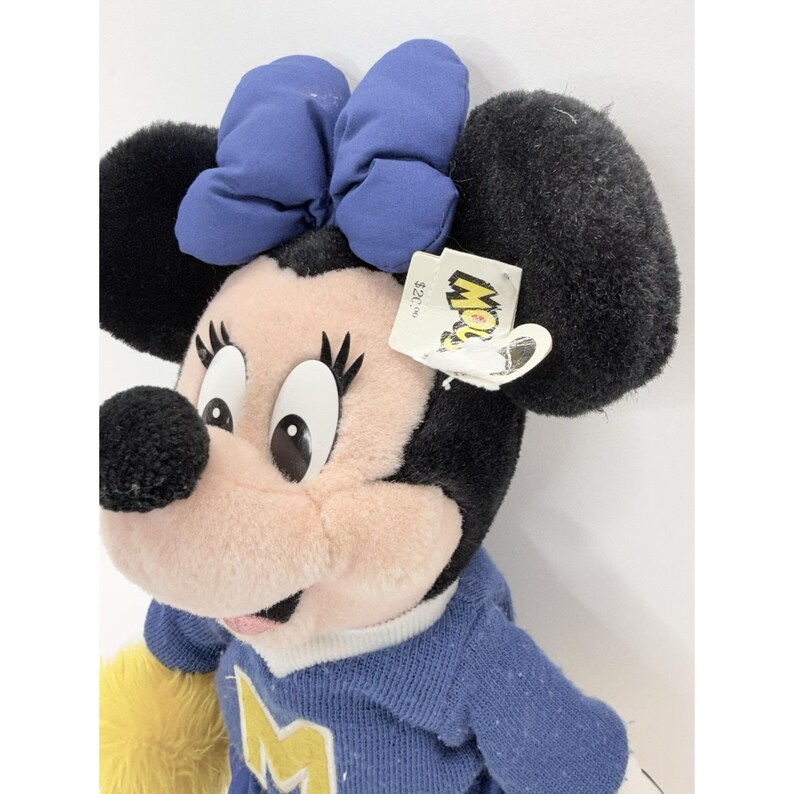 May include: A plush Minnie Mouse doll with a blue bow, black ears, and a blue sweater with a yellow accent. The doll has a tag that reads "Mow". The doll is a collectible item.