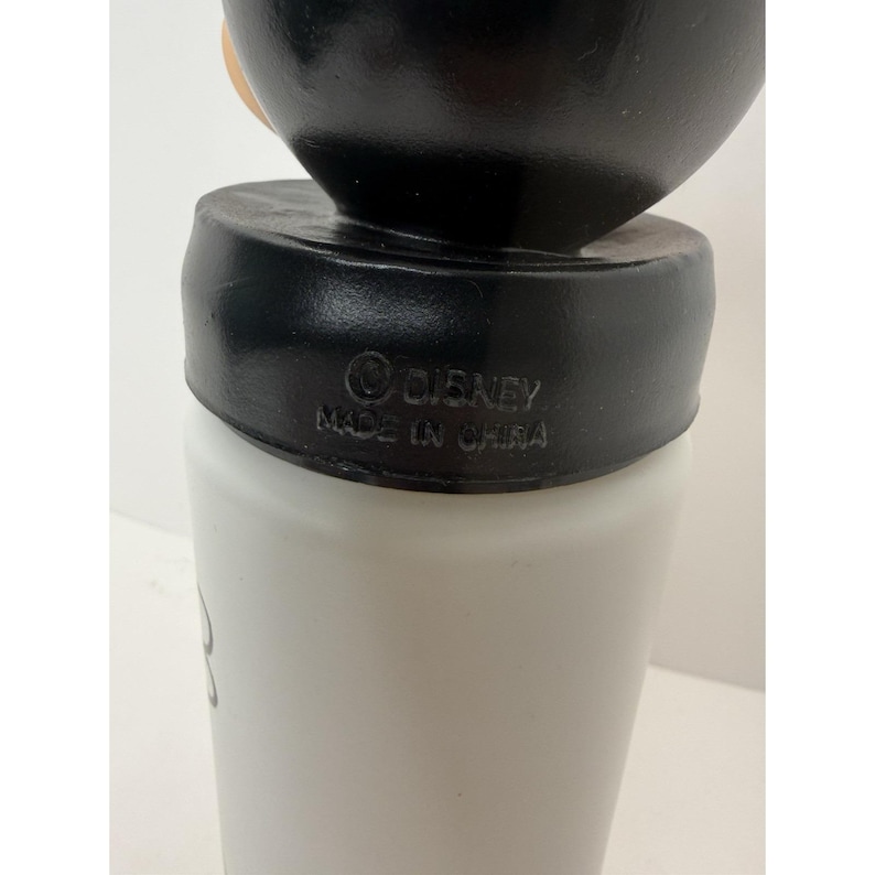 May include: A white and black Disney-branded tumbler. The tumbler has a black lid and a white body. The text "&copy; DISNEY MADE IN CHINA" is printed on the lid. The tumbler appears to be made of plastic.