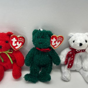 May include: Three plush teddy bears in red, green, and white. The red bear has a green bow, the green bear has a red bow, and the white bear has a red scarf with silver accents. Each bear has a heart-shaped tag.