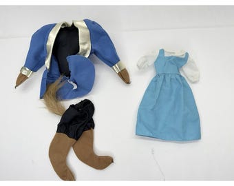 May include: A collection of doll clothing, including a blue jacket with gold trim, a blue dress with white sleeves, and black pants with brown boots. The items are arranged on a white surface.
