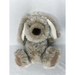 May include: A plush gray and brown dog toy with white ears. The dog is sitting with its paws in front of it.