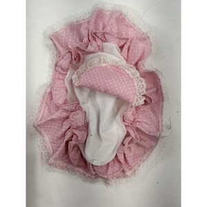 May include: A vintage baby doll diaper cover. The cover is pink with white polka dots and ruffled edges. A white mesh lining is visible inside. The edges are trimmed with white lace.