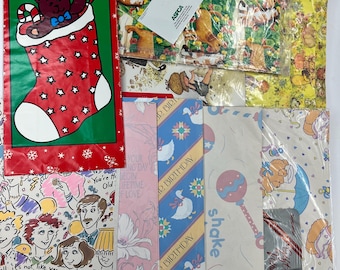 May include: A collection of colorful wrapping paper featuring various designs, including a teddy bear in a stocking, a birthday cake, a goose, and a baby rattle. The paper is packaged in plastic and includes a small card with the ASPCA logo.
