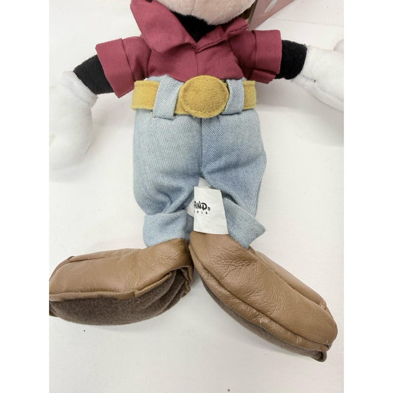 K&ouml;nnte beinhalten: Ein Pl&uuml;schtier einer Zeichentrickmaus mit einem weinroten Hemd, einer blauen Jeans und braunen Schuhen. Die Maus hat schwarze Handschuhe und wei&szlig;e H&auml;nde. Der G&uuml;rtel ist gelb. Ein Etikett mit dem Wort "AND" ist an der Jeans befestigt.