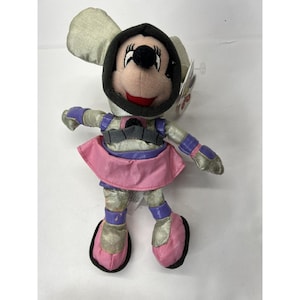 May include: A plush toy of Minnie Mouse dressed in a silver and purple space suit with a pink skirt. She has a black helmet with a white circle on the front.