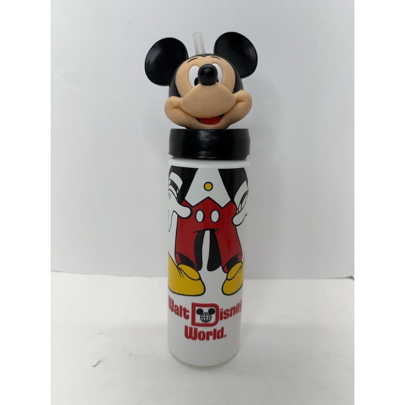 May include: A white water bottle featuring a Mickey Mouse design. The bottle has a black lid and a Mickey Mouse head on top. The bottle has a straw and the words "Walt Disney World" printed on it.