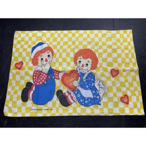 May include: A rectangular pillowcase featuring a yellow and white checkered pattern. The design displays two rag dolls with red yarn hair, one wearing blue overalls and the other a blue floral dress, holding a red heart printed with I LOVE YOU.