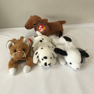 May include: Four plush toys, a brown cat, a brown and white dalmatian dog, a black and white dog, and a brown dachshund dog. All of the toys have red and white Ty tags.