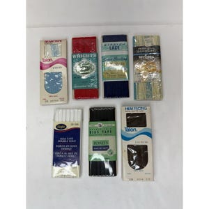 May include: Assortment of sewing notions including seam tape, bias tape, and hem facing. The items are packaged in various colors, including red, blue, black, and white. Brands include Wrights, Talon, and Penney's.